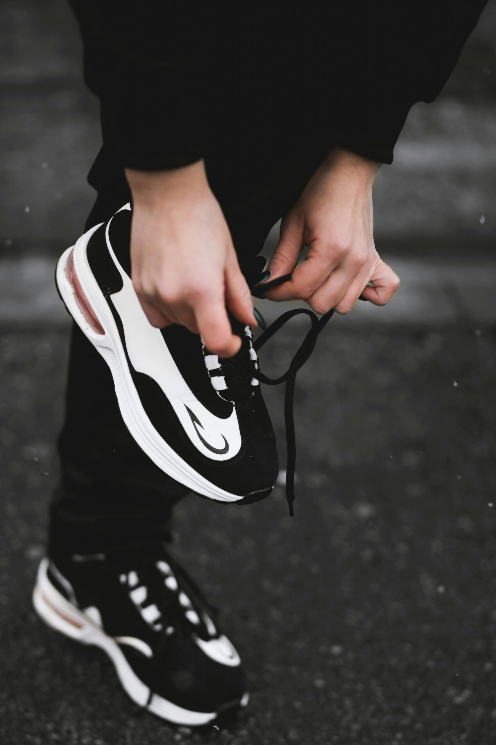 Close-up of a person tying the laces on a black-and-white athletic sneaker while standing on a pavement.